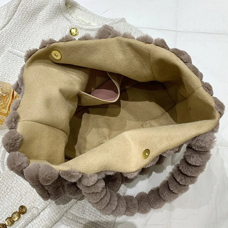 Close-up of a beige handbag with gray pom-pom trim on a white background