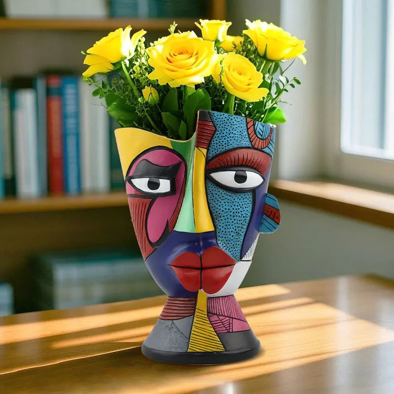 Colorful face-shaped vase with yellow roses on a wooden surface