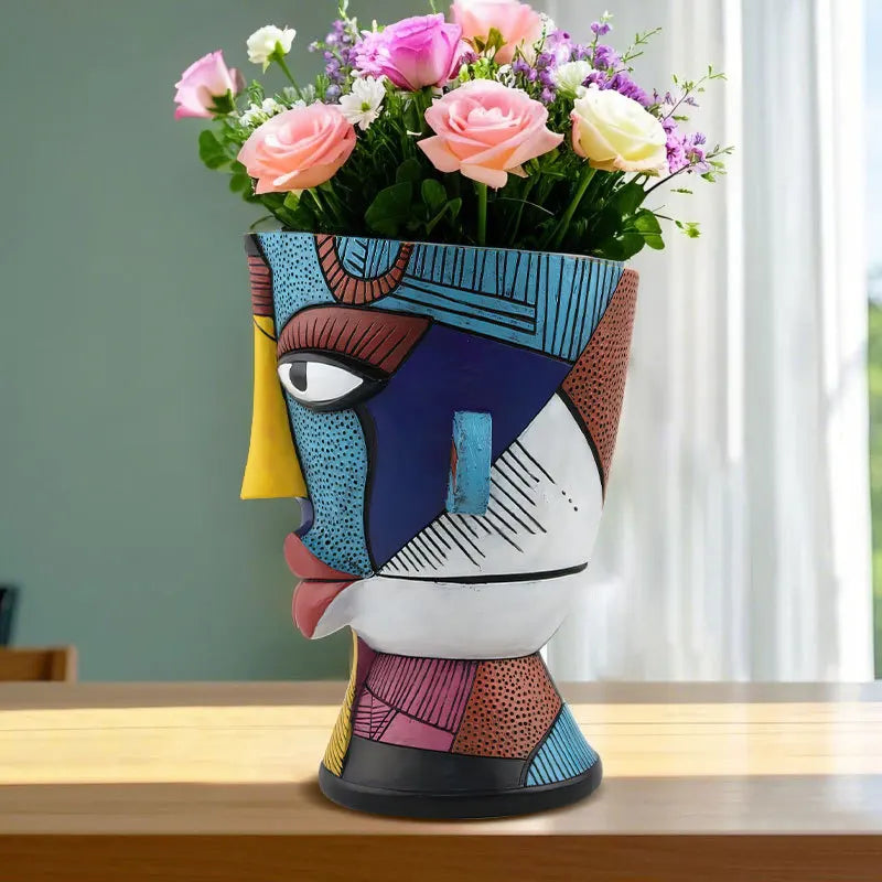 Colorful abstract vase with a face design holding flowers on a wooden surface.