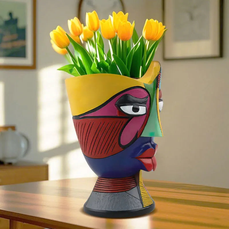 Colorful vase shaped like a face with yellow tulips on a wooden table.