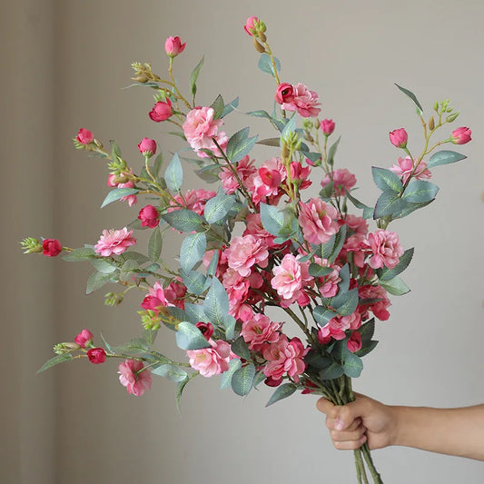 Bouquet of pink flowers held by a hand against a neutral background