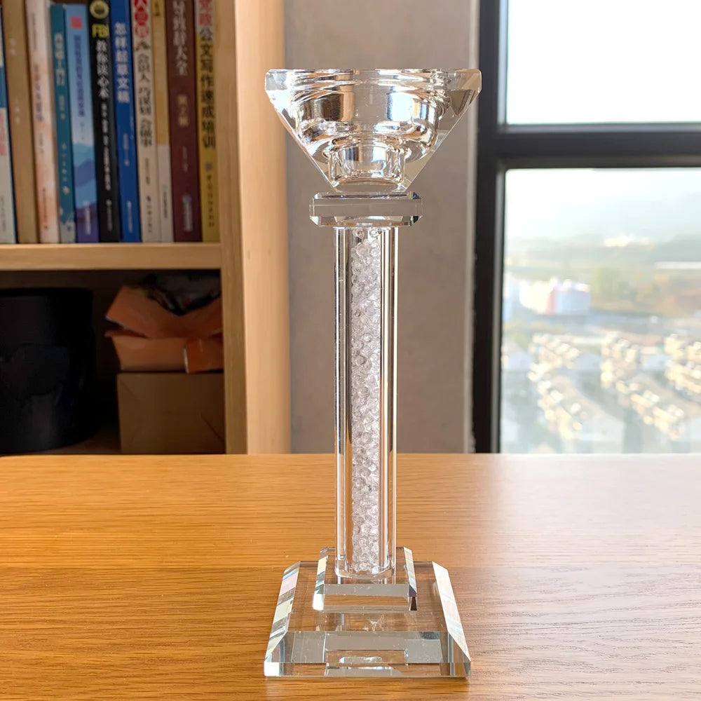 Clear crystal candle holder with crystal pieces in the column, on a wooden surface with books and a window in the background