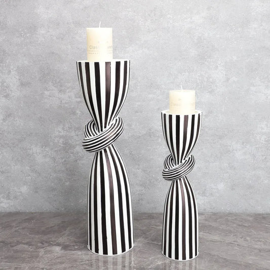 Two black and white striped candle holders with candles on a gray surface and background.