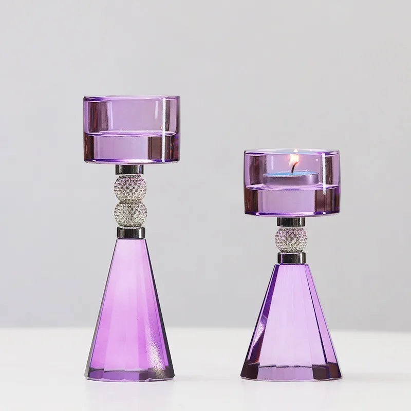 Two purple glass candle holders with geometric cone-shaped bases and cylindrical cup holders, one unlit and one lit with a candle, set against a plain light gray background.