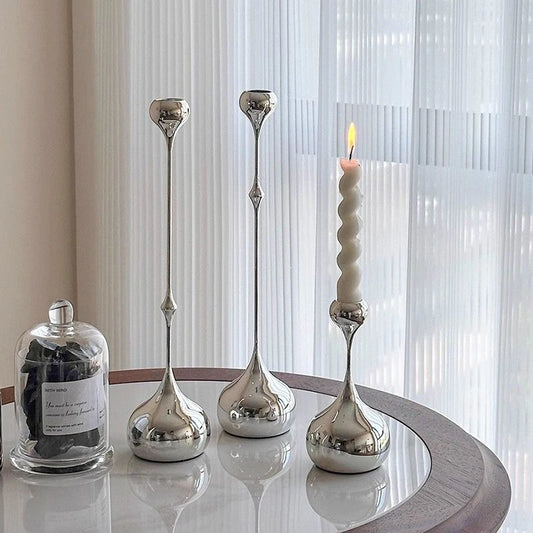 Set of silver candle holders on a reflective surface with a curtain background