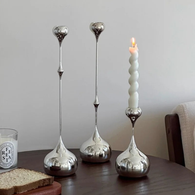 Three silver candle holders on a table with a lit candle and a glass of milk.