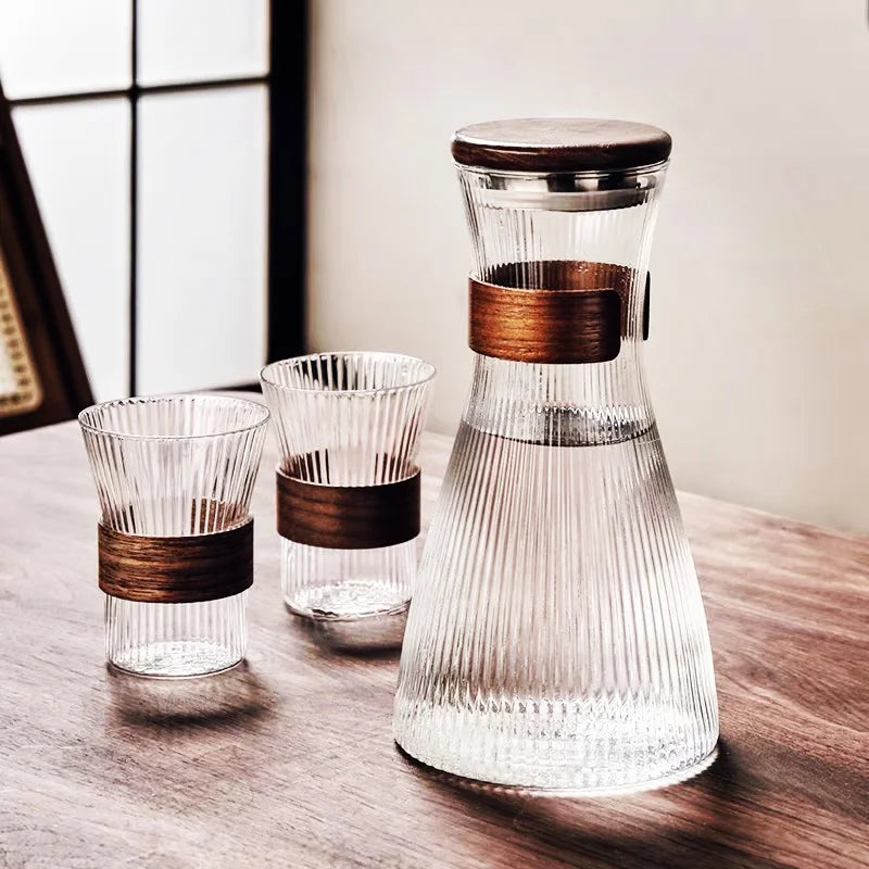 Ribbed glass carafe with wooden bands and matching glasses on a wooden surface.