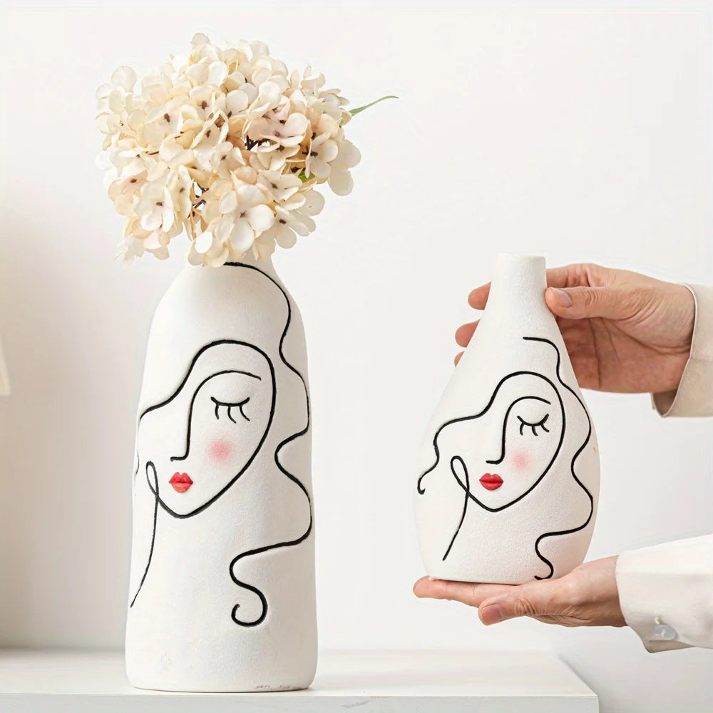 Two white vases with face designs holding flowers on a light background