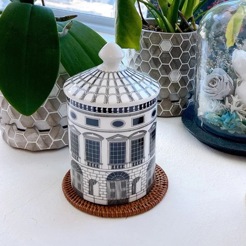 Decorative jar with architectural design on a white surface with plants in the background