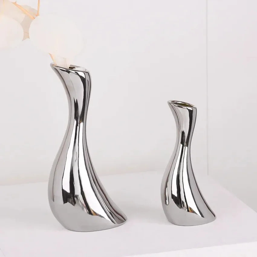 Two modern metallic silver ceramic vases with a reflective, curved design, displayed on a white surface against a white background.