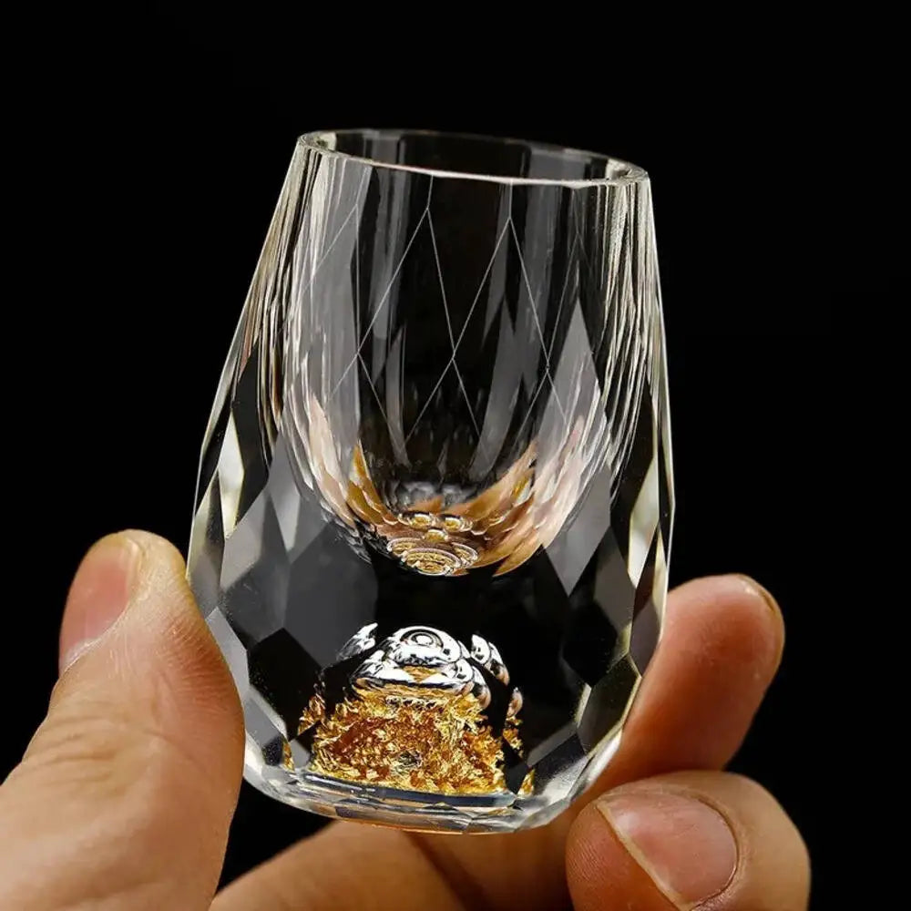 Clear glass with gold interior held by a hand against a black background
