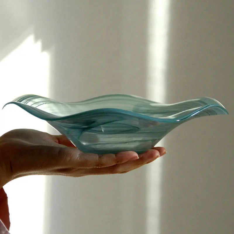 Hand holding a wavy blue glass bowl against a white background