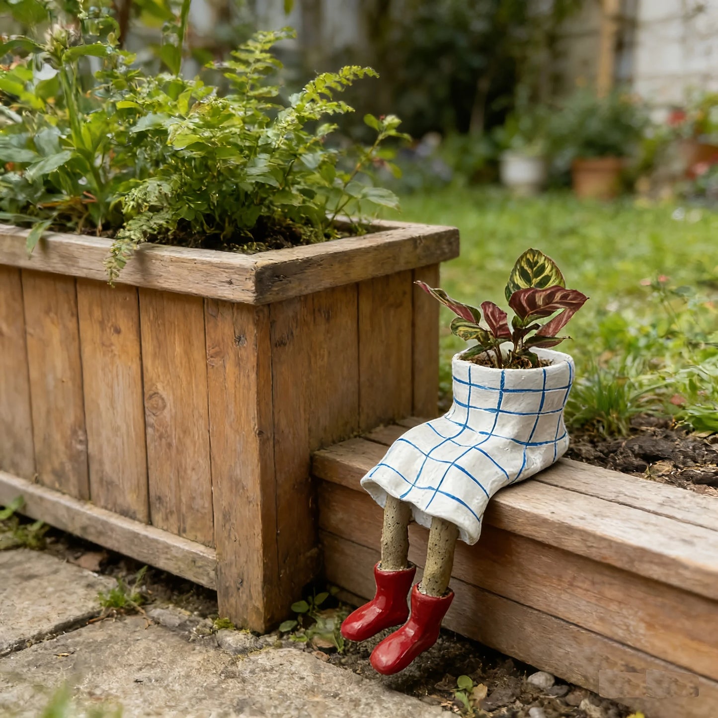 Small garden pot in a plaid outfit and red boots sitting on a wooden planter with plants.
