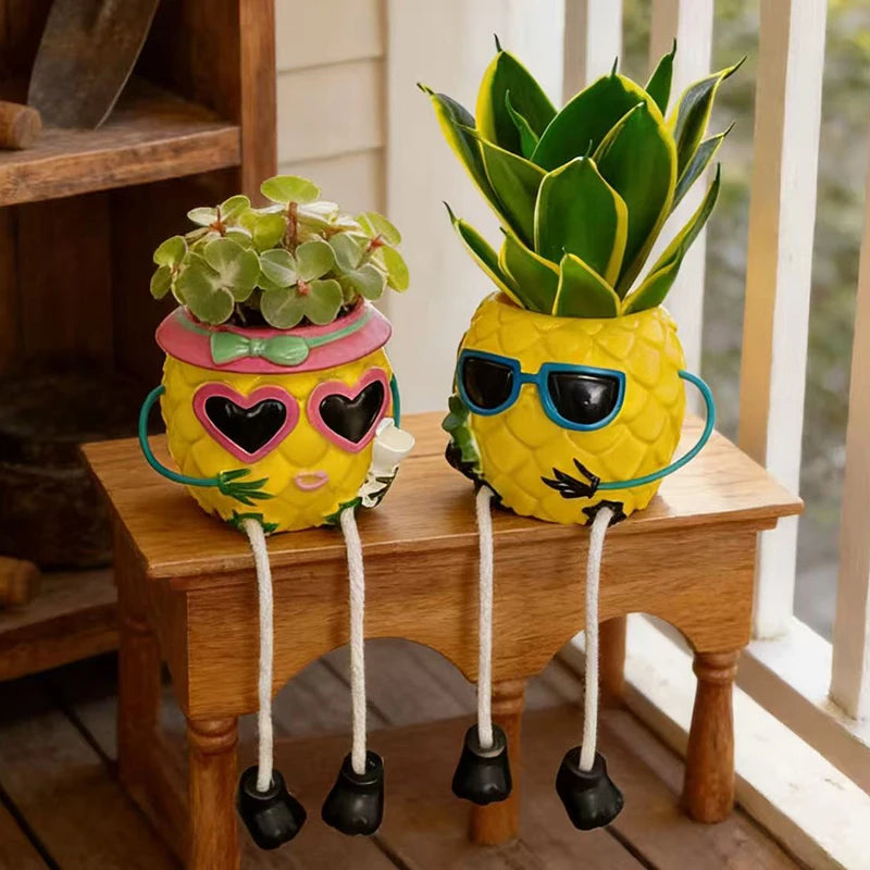 Two pineapple-shaped planters with legs and sunglasses sitting on a wooden bench. The left planter has a small green succulent and wears pink heart-shaped sunglasses and a pink bow.