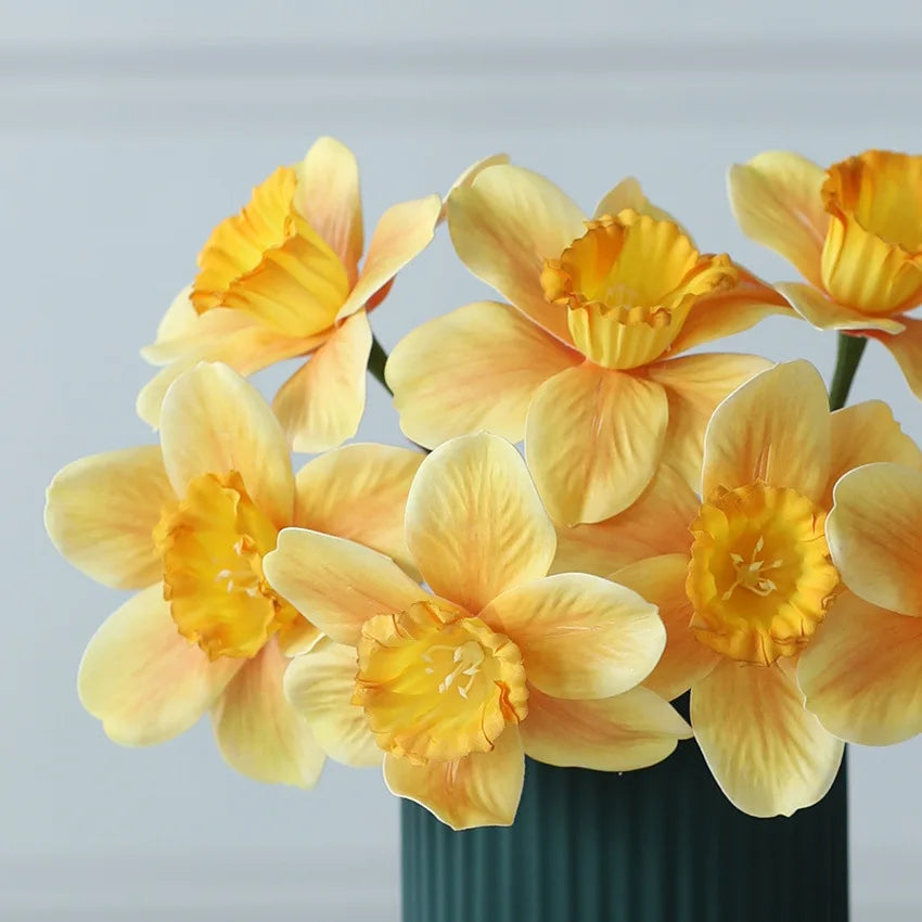 Yellow daffodils in a green vase against a light gray background