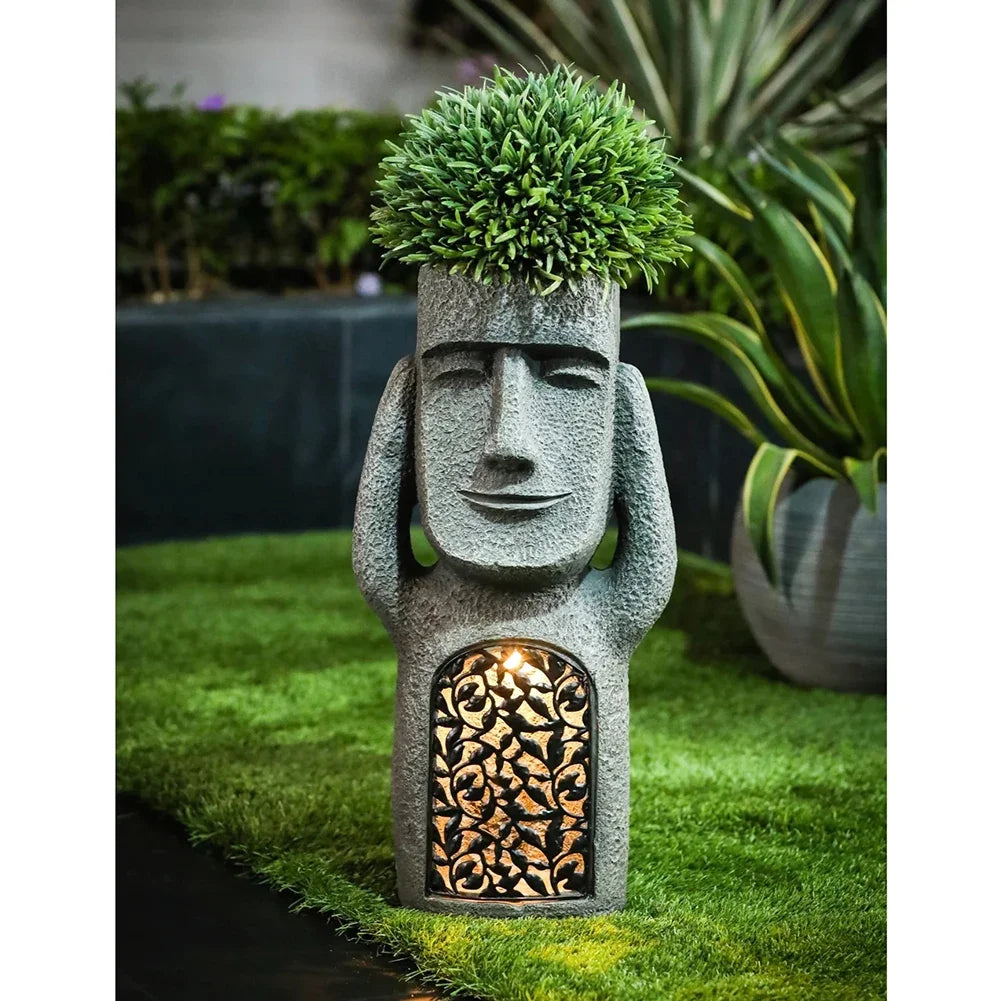 Garden statue - hear no evil - with face and plant on head, illuminated from inside, on grass.