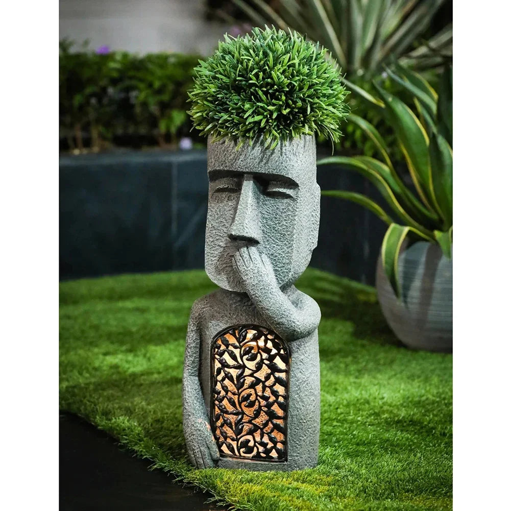 Garden statue with face and floral topiary on grass - speak no evil