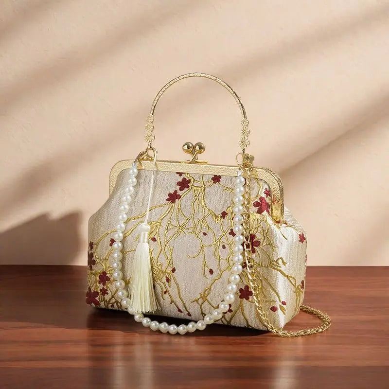 Decorative handbag with floral embroidery and pearl chain on a wooden surface.