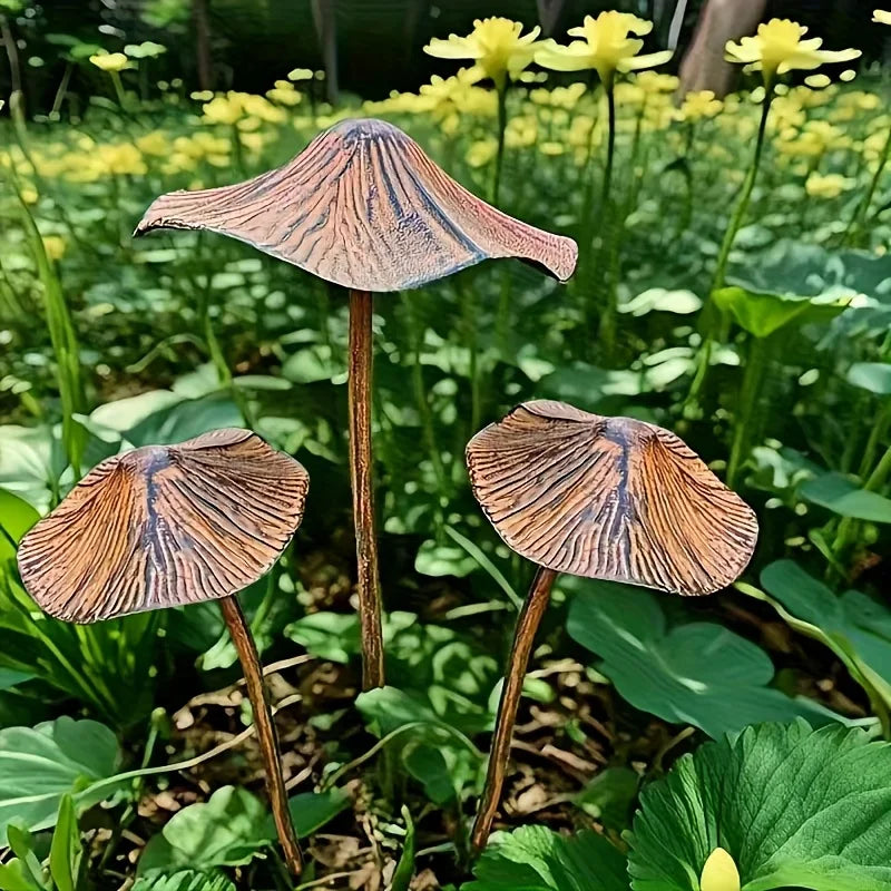 Three decorative mushroom sculptures in a garden setting with greenery and yellow flowers.
