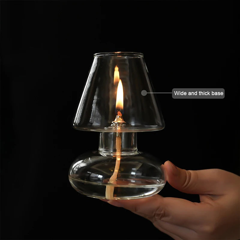 Hand holding a clear glass oil lamp with a flame against a black background