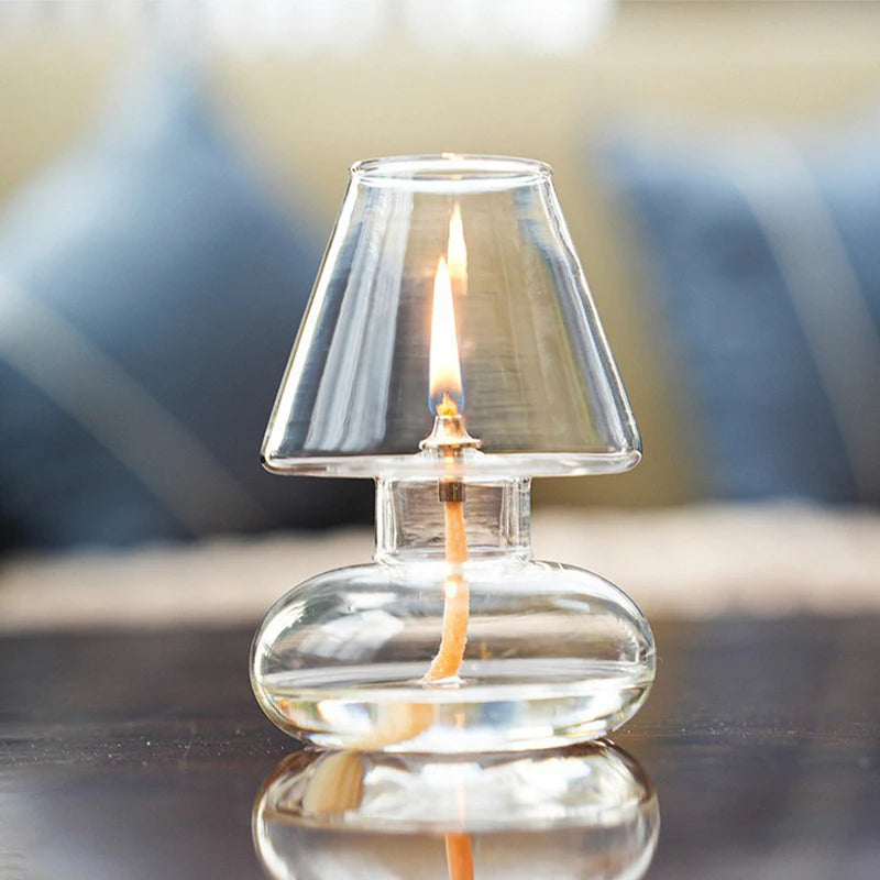 Clear glass lamp with a candle inside on a reflective surface.