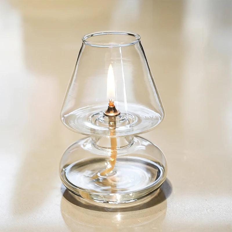 Clear glass oil lamp with a lit wick on a neutral background