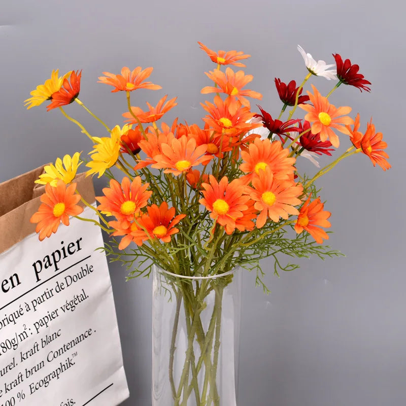 Bouquet of orange, yellow, and red flowers in a clear vase on a gray background.