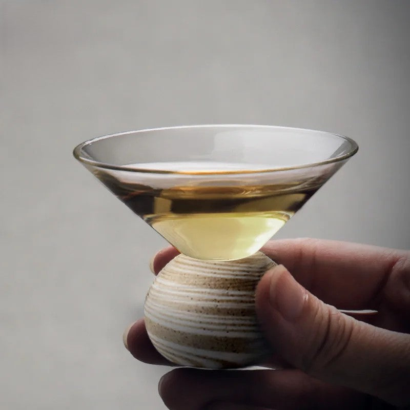 Hand holding a small glass container with a liquid inside against a gray background