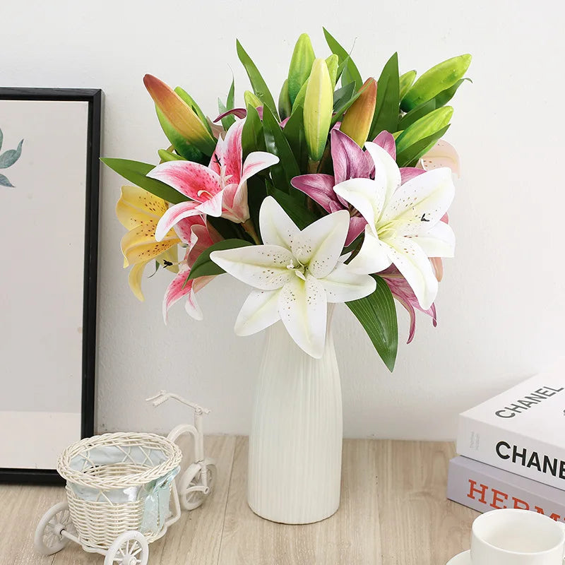 Bouquet of colorful lilies in a white vase on a wooden surface with books and a framed picture in the background.