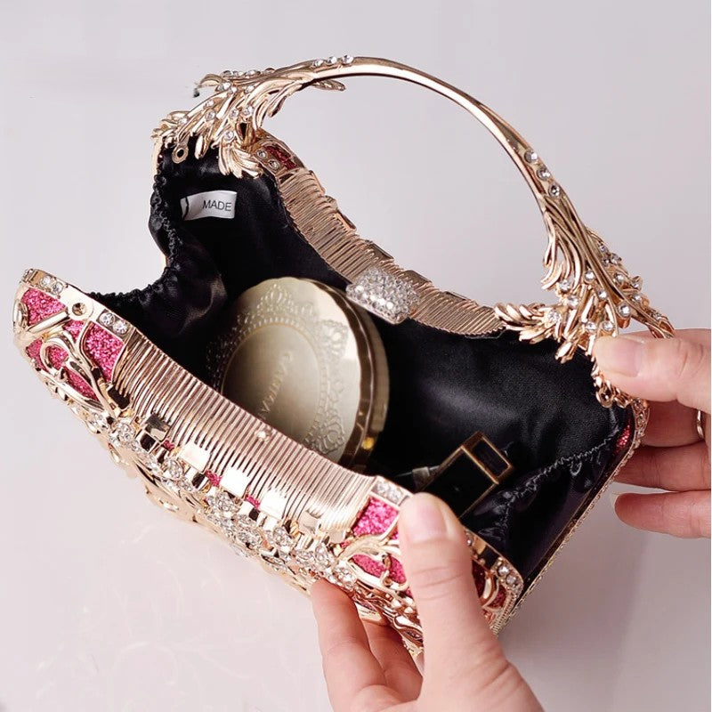 Gold and pink handbag with a decorative handle held by a hand against a light gray background