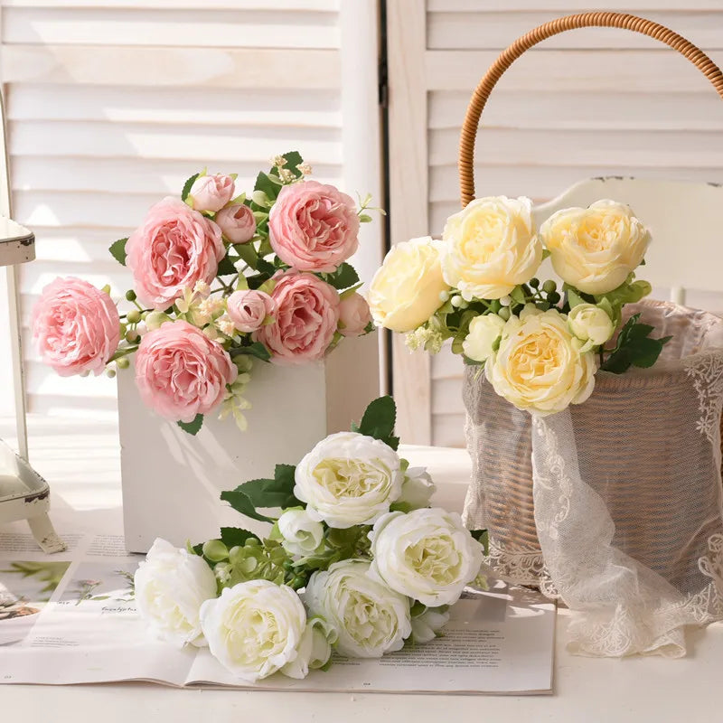 Three bouquets of pink, yellow, and white Peonies on a table with a wicker basket in the background.