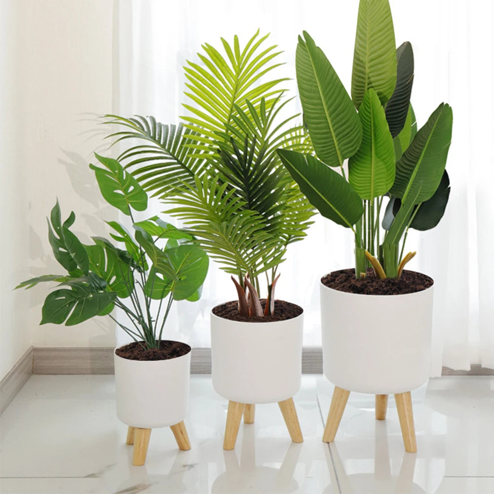 Three potted plants in white pots with wooden legs on a light floor.