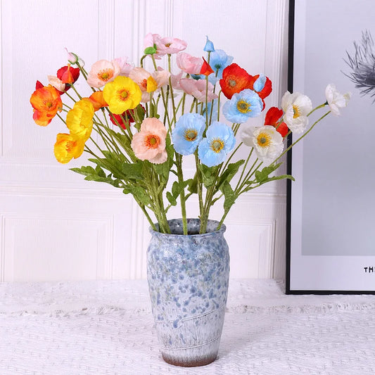 Colorful artificial flowers in a decorative vase on a white surface.