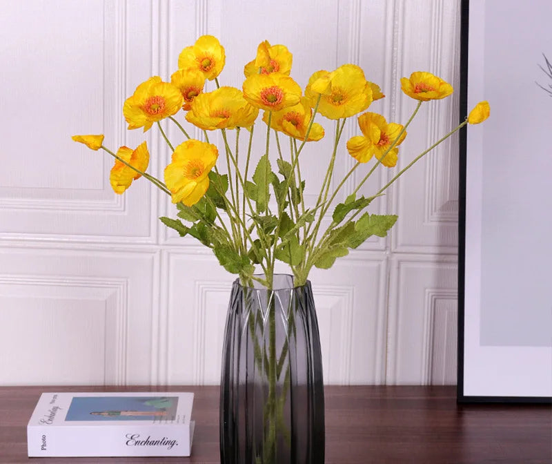 Yellow flowers in a black vase on a wooden surface with a white paneled wall background