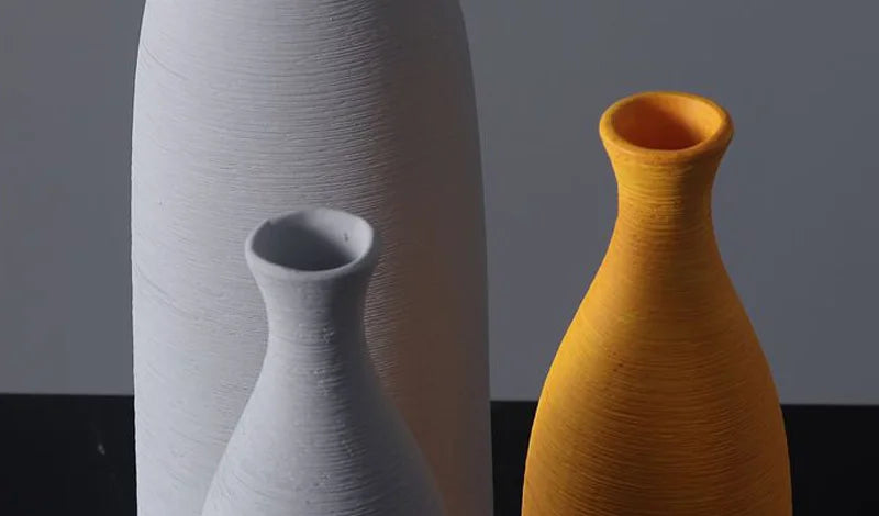 Three textured ceramic vases in white and mustard yellow, arranged against a dark gray background.