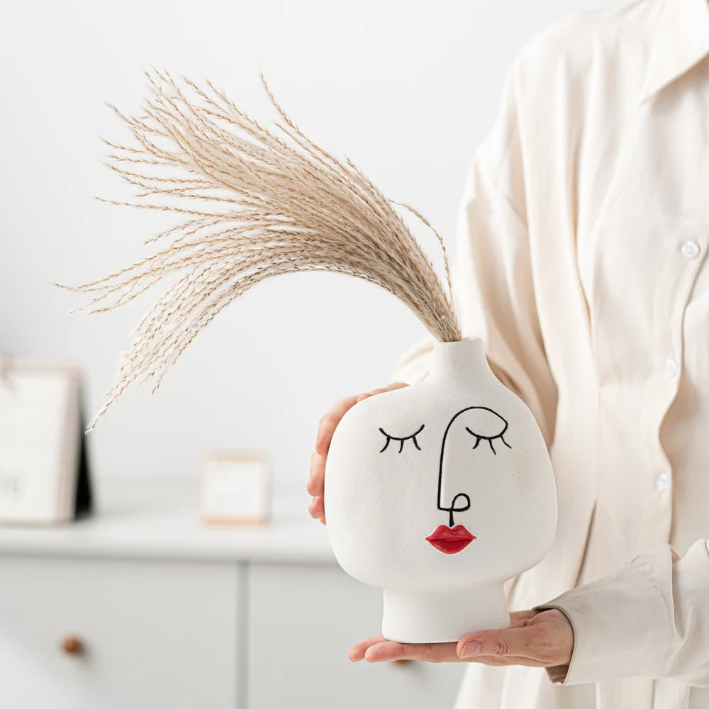 Person holding a white vase with a face design against a light background