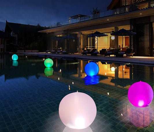 Colorful illuminated balloons floating in a pool at night with a house in the background.