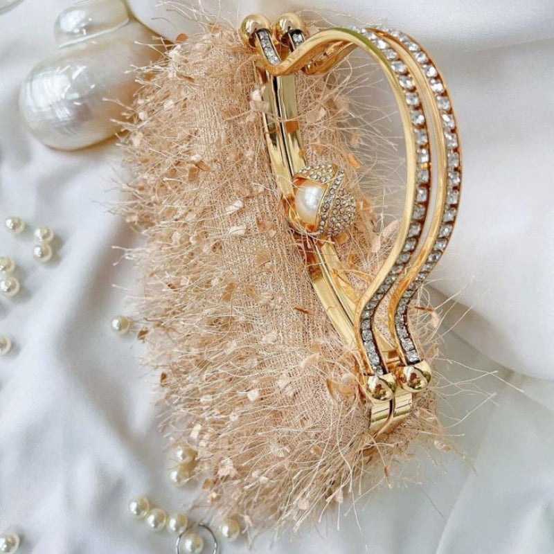 Gold clutch bag with pearl closure on a textured surface