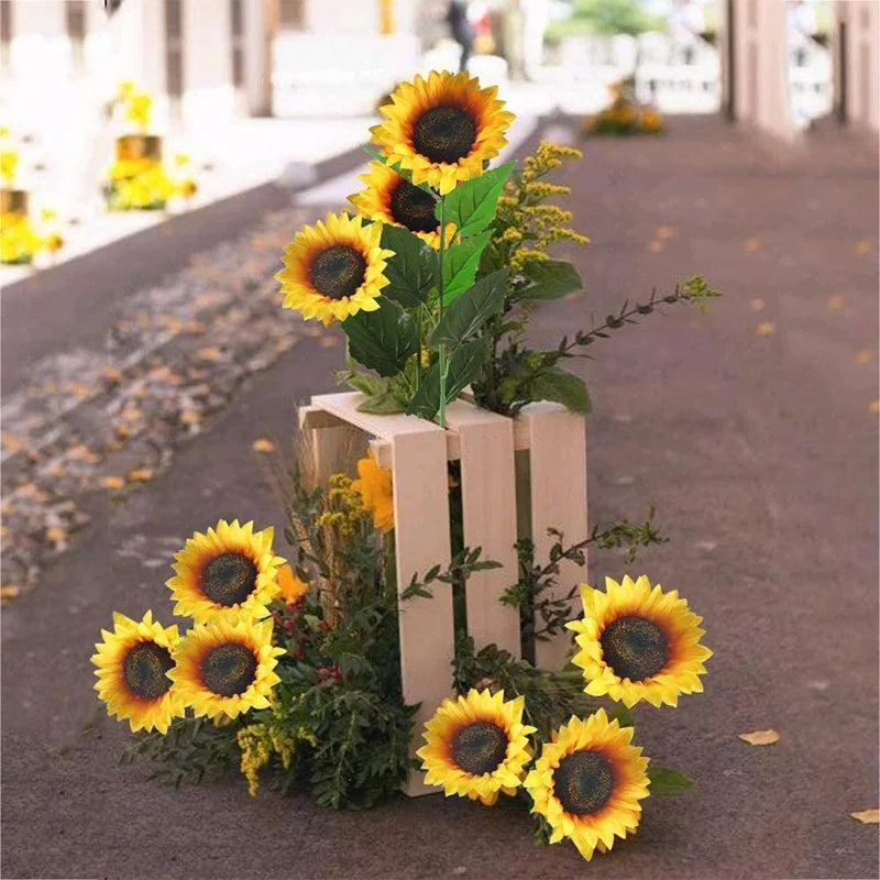 Artificial sunflowers and greenery arranged in a wooden box on a pavement.