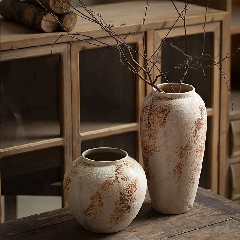 Two rustic ceramic vases on a wooden surface with a wooden cabinet in the background.