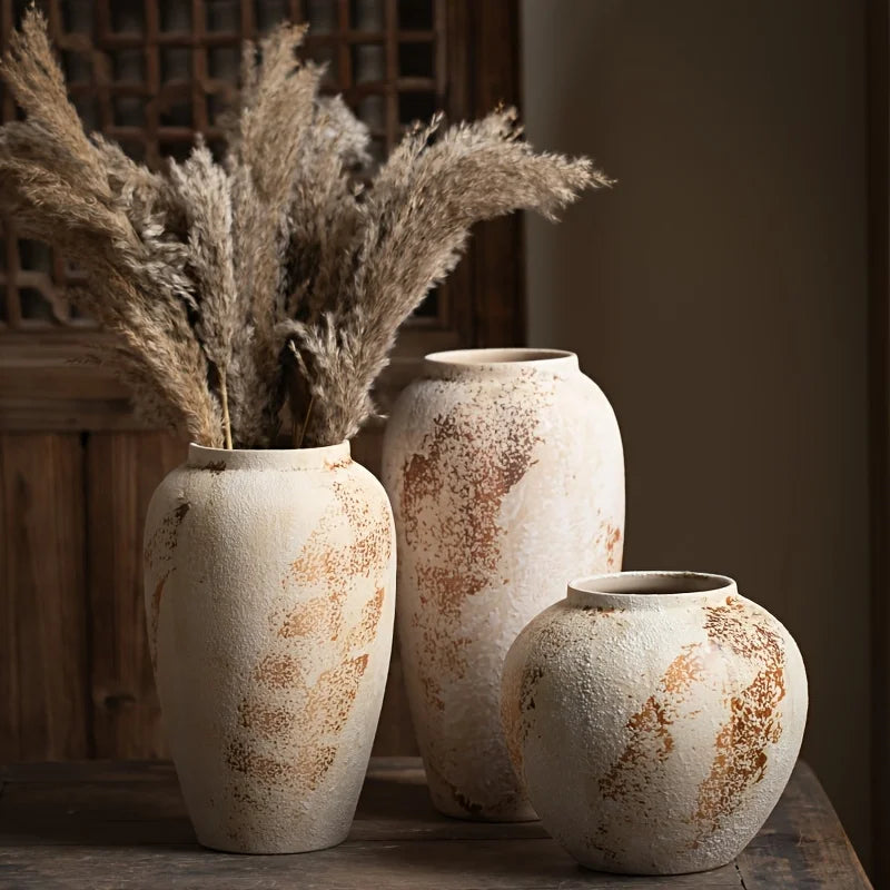 Three rustic ceramic vases with dried plants on a wooden surface.