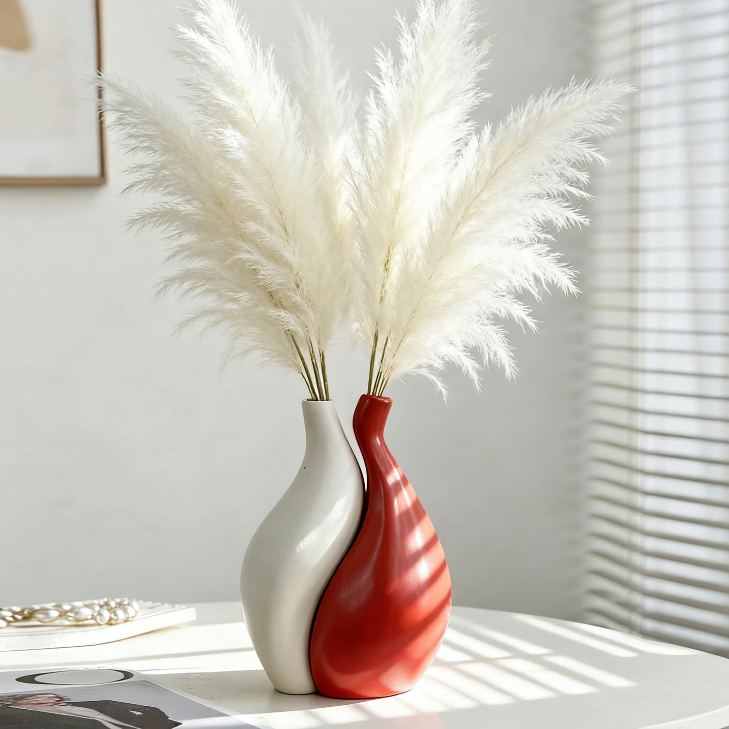 Two-tone ceramic vase with white and red design, containing dried pampas grass on a light surface.
